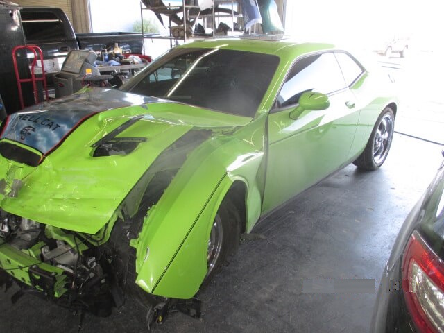 Before repair of a green car with fender and bumper damage.