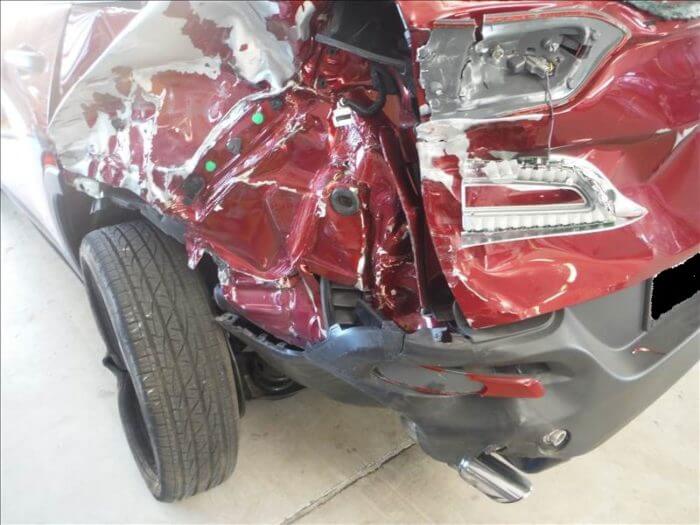 Before repair of a red car with major rear bumper and trunk damage.