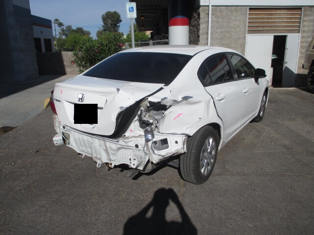 Before repair of a white car with rear bumper and quarter panel damage.